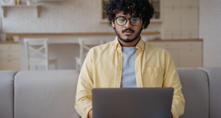 Pensive Indian man using laptop computer searching online looking at digital screen