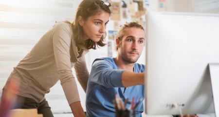 Woman and man at a desk looking at something on a monitor