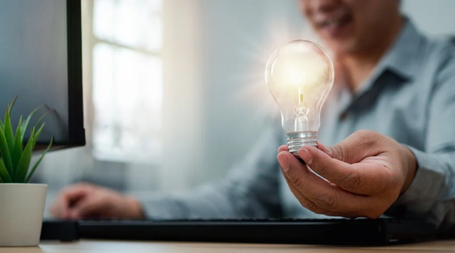 a man holding a lightbulb whilst using a computer