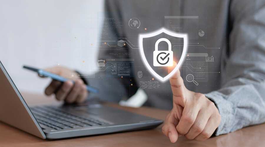 a man on a laptop touching a holographic image of a shield with a padlock in it
