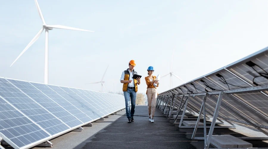 two people walking between solar panels and wind turbines